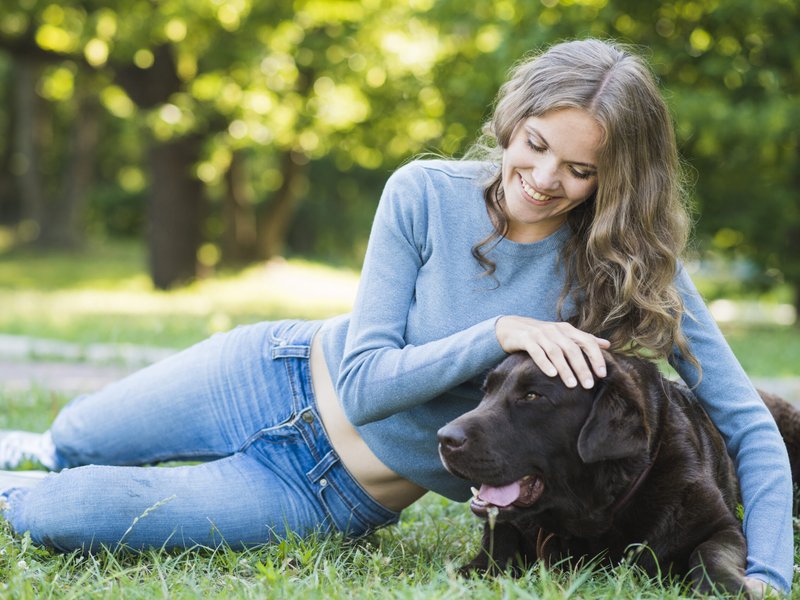 Happy young woman leaning with dog on green grass